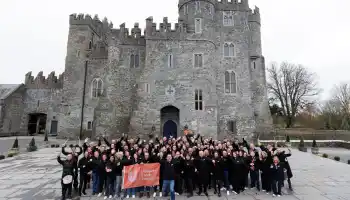 Corporate leadership team building event in Ireland with large group celebrating outside a historic castle venue