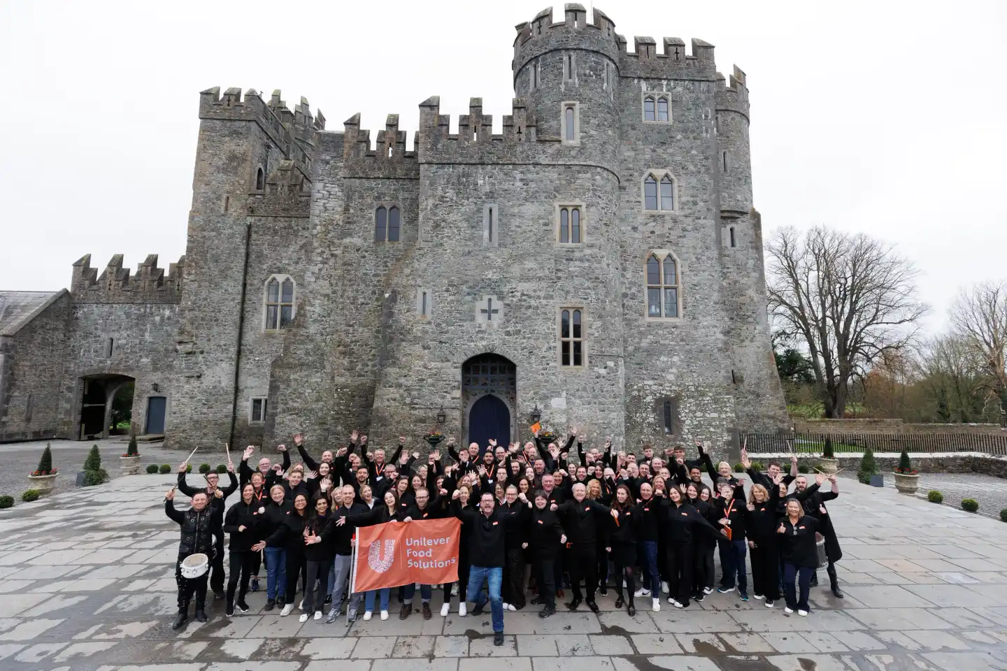 Corporate leadership team building event in Ireland with large group celebrating outside a historic castle venue