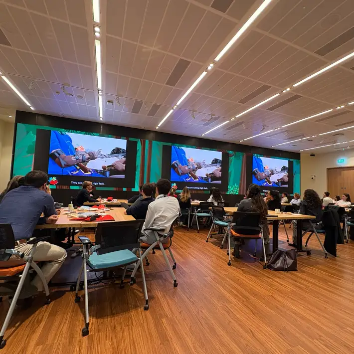 Corporate team in Ireland watching an impact video showing prosthetic hand recipients during The Hand Project CSR team building workshop.