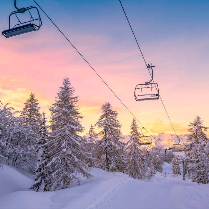 Snowy ski lift at sunrise surrounded by pine trees, representing the winter setting of the Murder on the Slopes virtual team building game in Ireland.